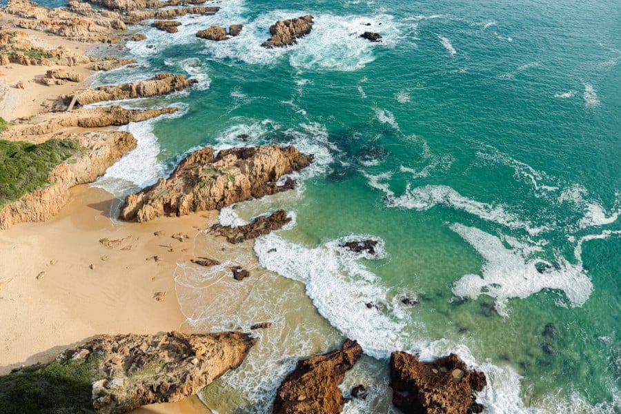 Aerial view of waves breaking over rocky outcrops on a sandy coastline