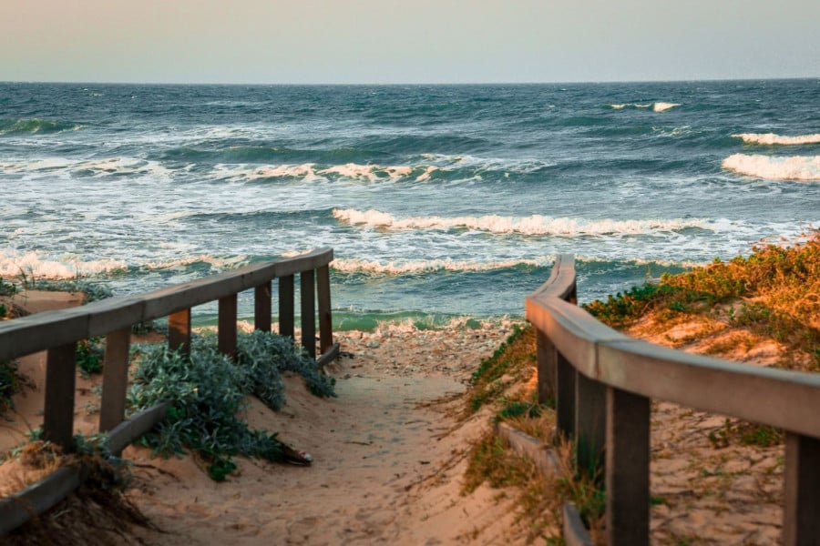 Wooden boardwalk leading through sand dunes towards waves breaking on a beach in Gqeberha