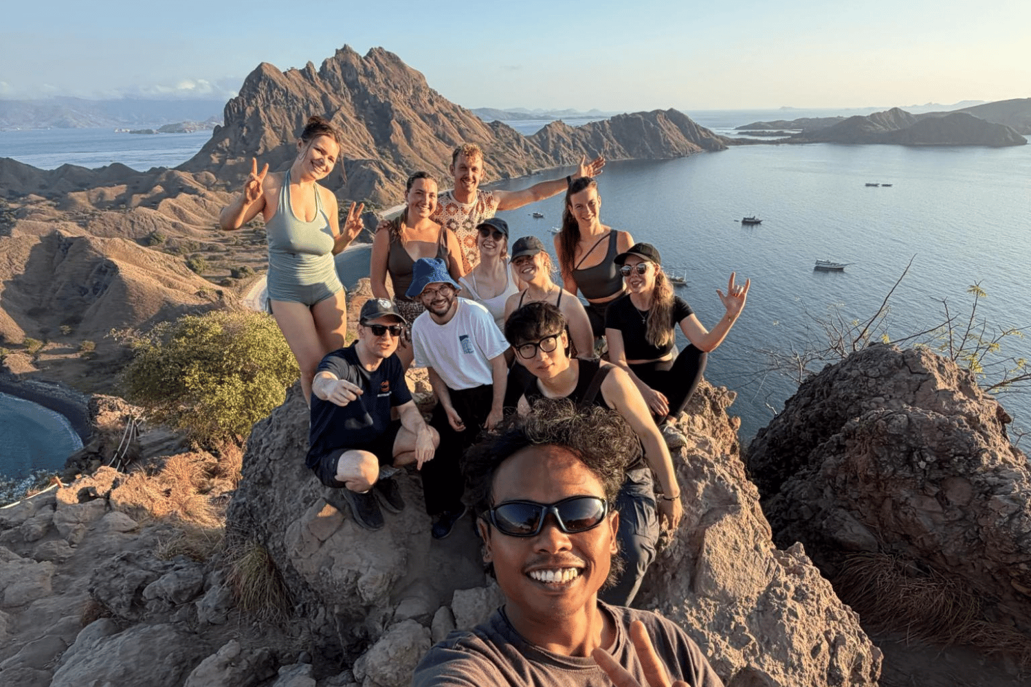 Group of people posing for a selfie on a rocky hilltop above the sea at sunset Padar Island