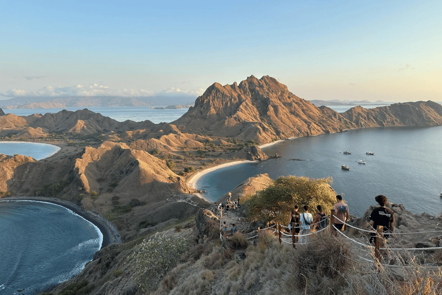 People standing on a rocky viewpoint overlooking bays and boats at sunset at Padar Island