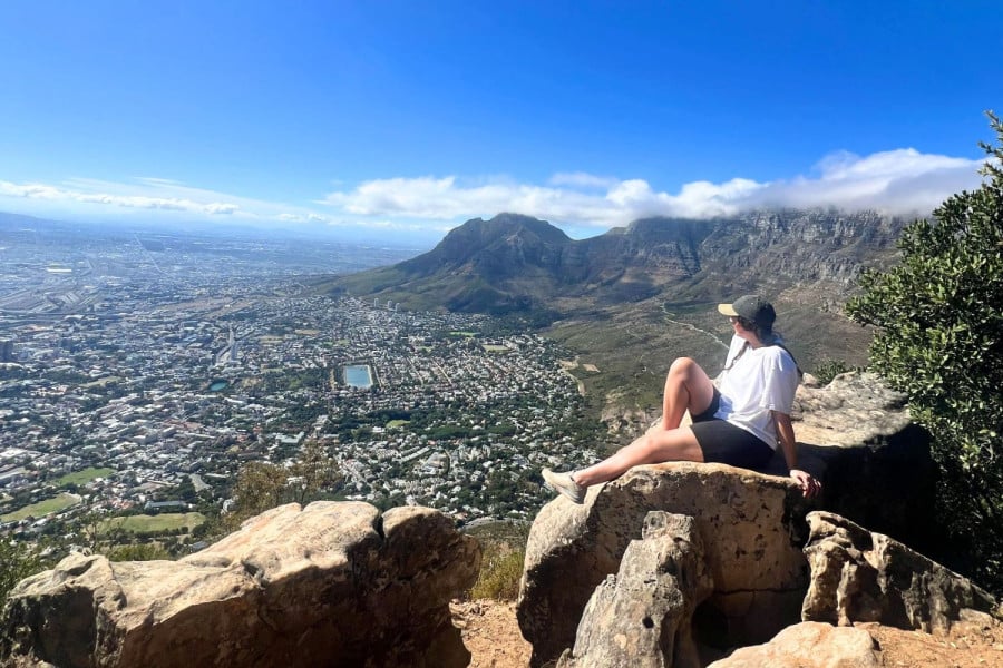 Person sitting on a rock overlooking a city and mountain range in Cape Town, South Africa