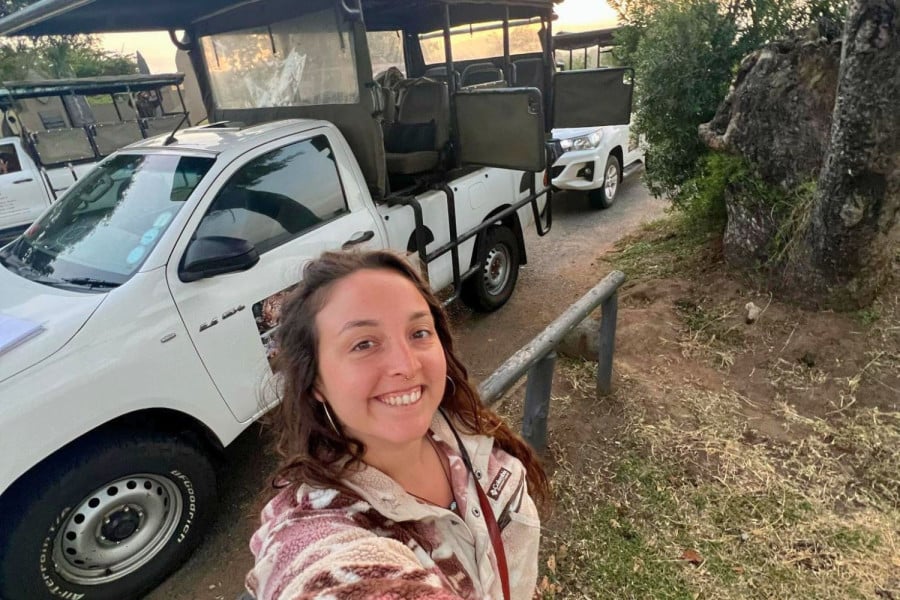 Smiling person taking a selfie beside open safari vehicles on a dirt track